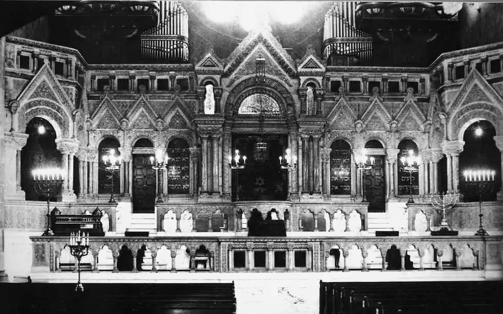 Innenraum einer historischen Synagoge mit Toraschrein, Menoras und kunstvollen Verzierungen.